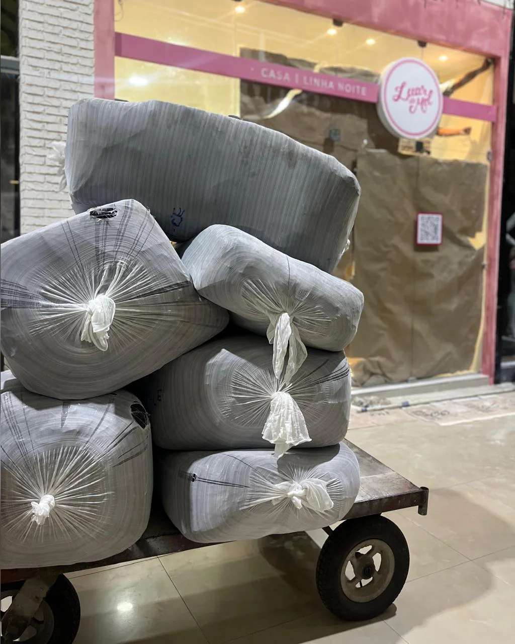 Fardos de tecido embalados sobre um carrinho, prontos para envio, em frente à loja LUAR DE MEL®